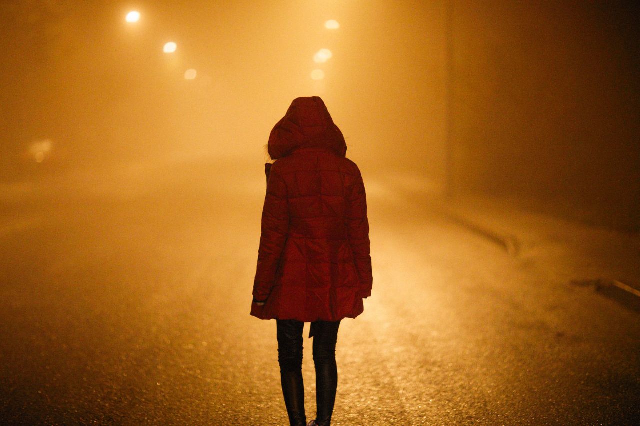 a mysterious silhouette in a red coat stands under streetlights on a f