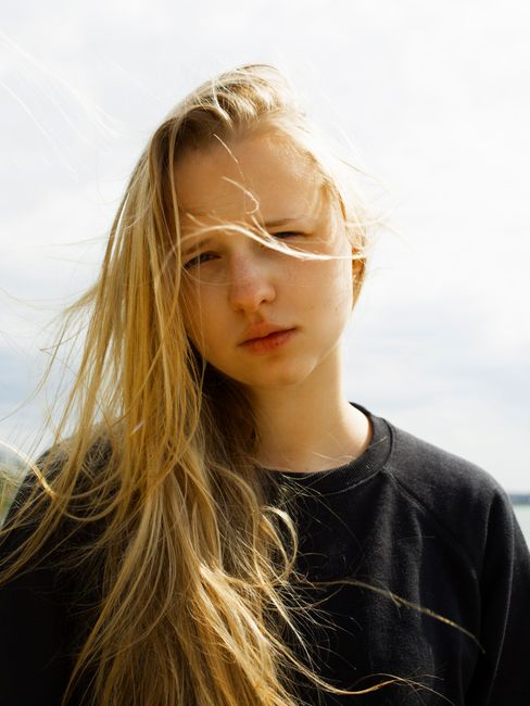 Intimate portrait of a young woman with windblown hair, conveying a sense of freedom and introspection.