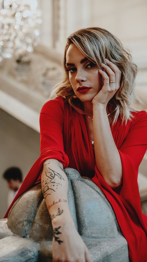 Free Elegant woman in red dress indoors with tattoos on arm. Moody lighting, stylish setting. Stock Photo
