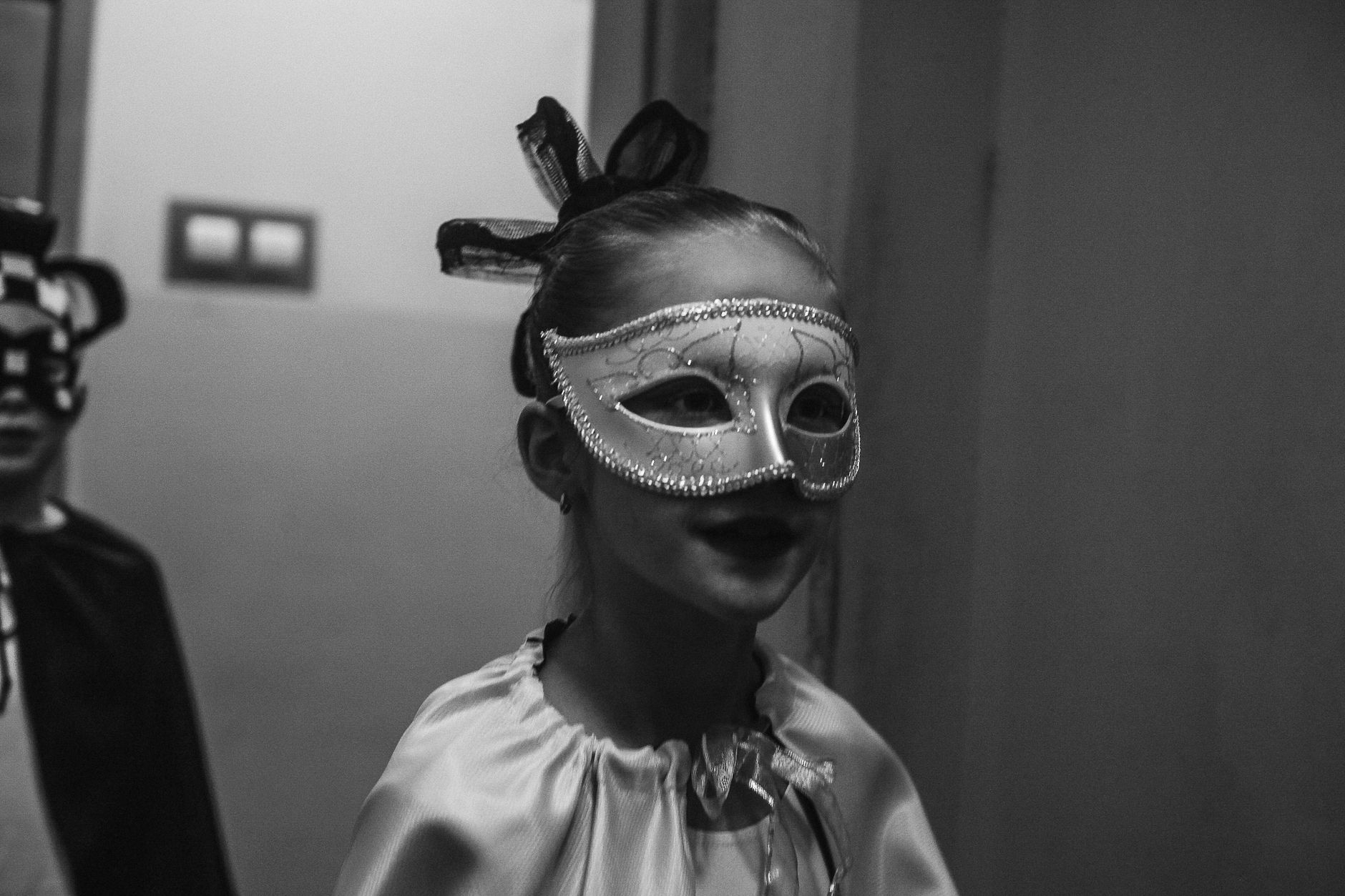 A child in a masquerade mask and costume, captured in black and white, exuding a playful and mysterious aura.