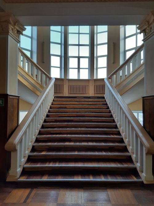 Free Elegant wooden staircase with balusters and large windows indoors, creating a classic architectural look. Stock Photo