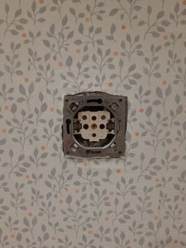 Uncovered electrical socket on patterned wallpaper showcasing home renovation or electrical work.