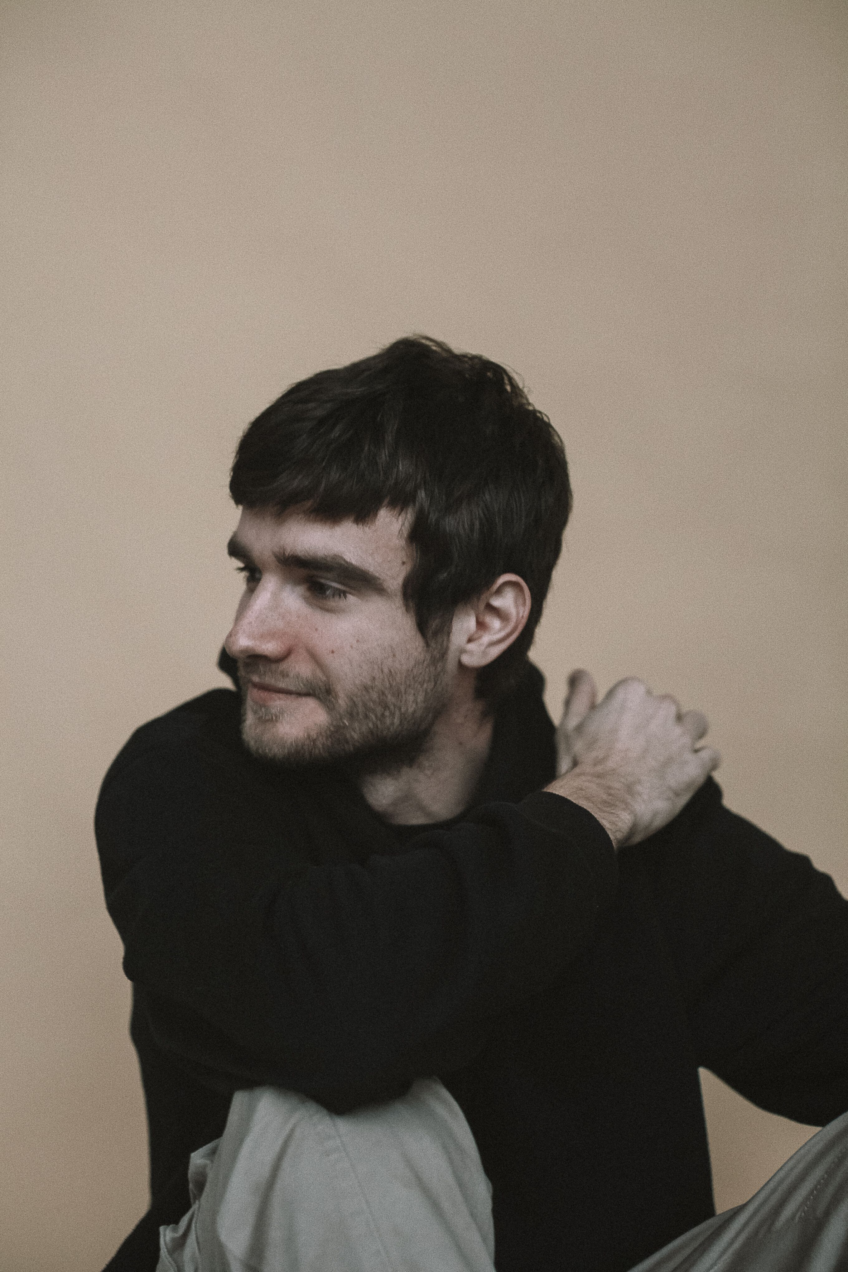 A contemplative portrait of a bearded man in casual black attire looking over his shoulder.
