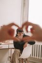 View of Young Man Sitting with Crossed Legs in Chair within Heart Made of Unrecognizable Hands