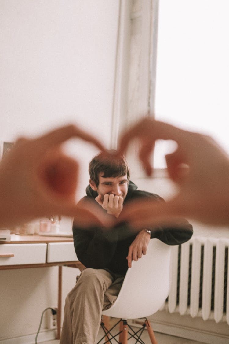 View Of Young Man Sitting With Crossed Legs in Chair Within Heart Made Of Unrecognizable Hands