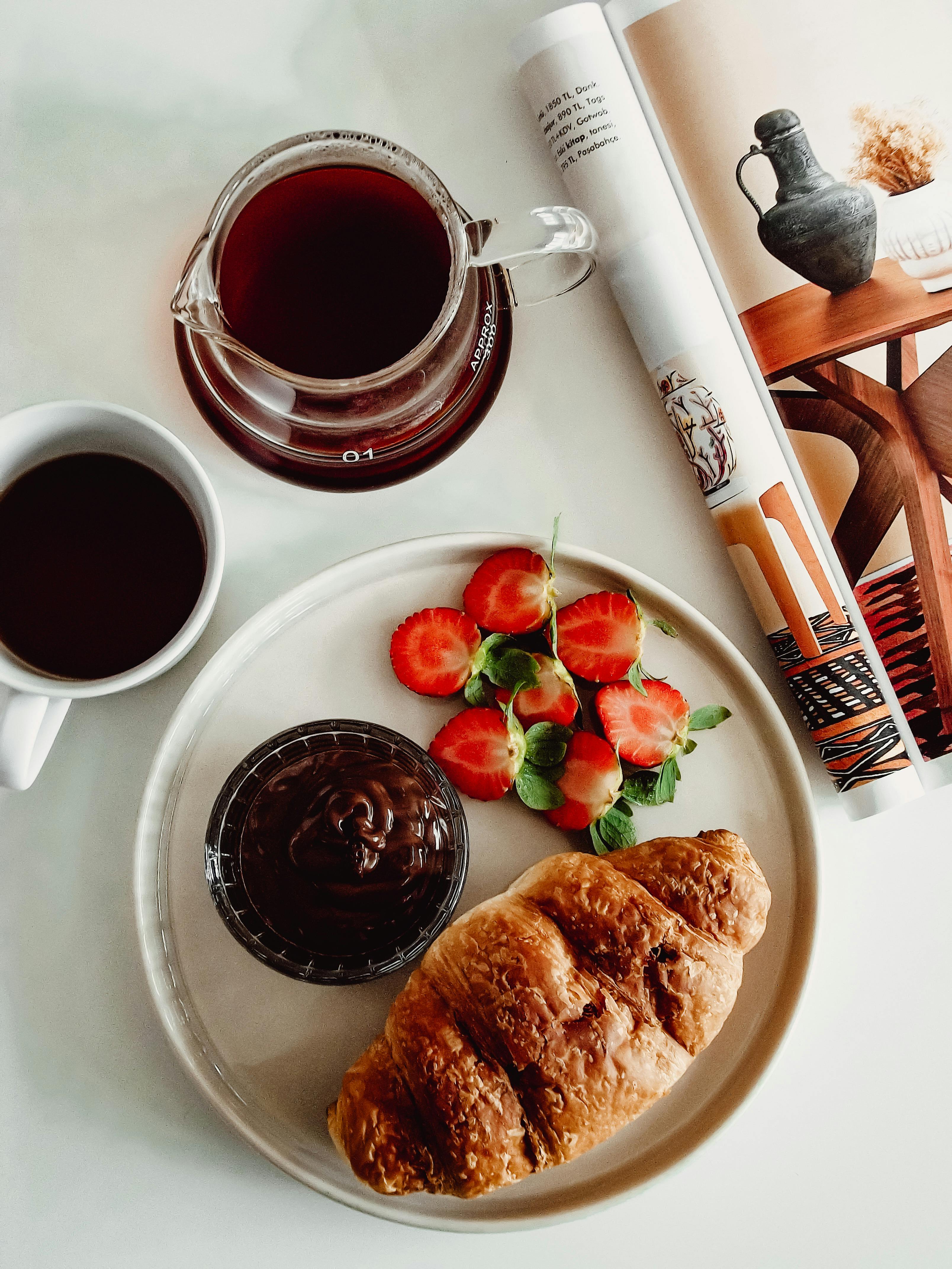 Top view of a breakfast with croissant, coffee, strawberries, and a magazine.