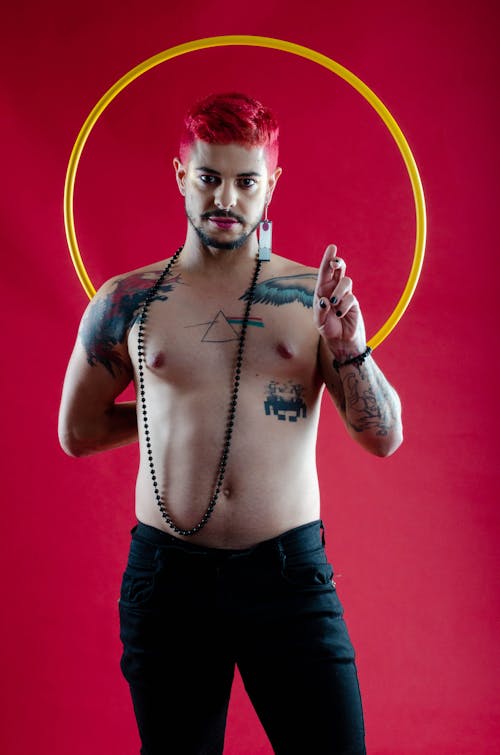 Shirtless Man with Tattoos and Red Dyed Hair, Posing against Red Background