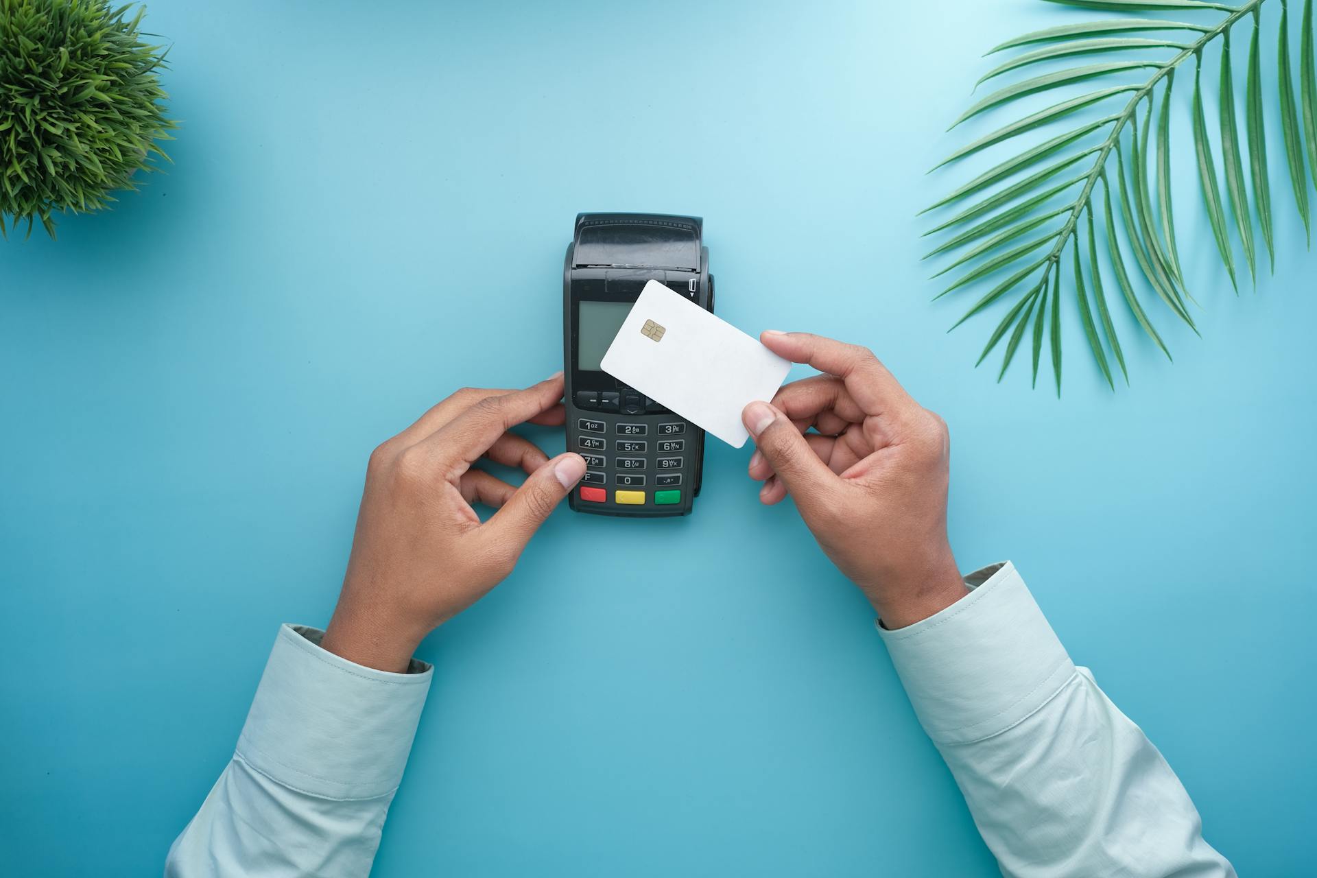 Hands using a contactless credit card on a payment terminal with a stylish minimal background.