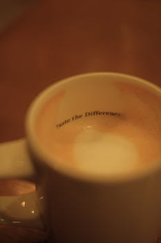 Close-up of a white mug filled with frothy cappuccino featuring text inside.