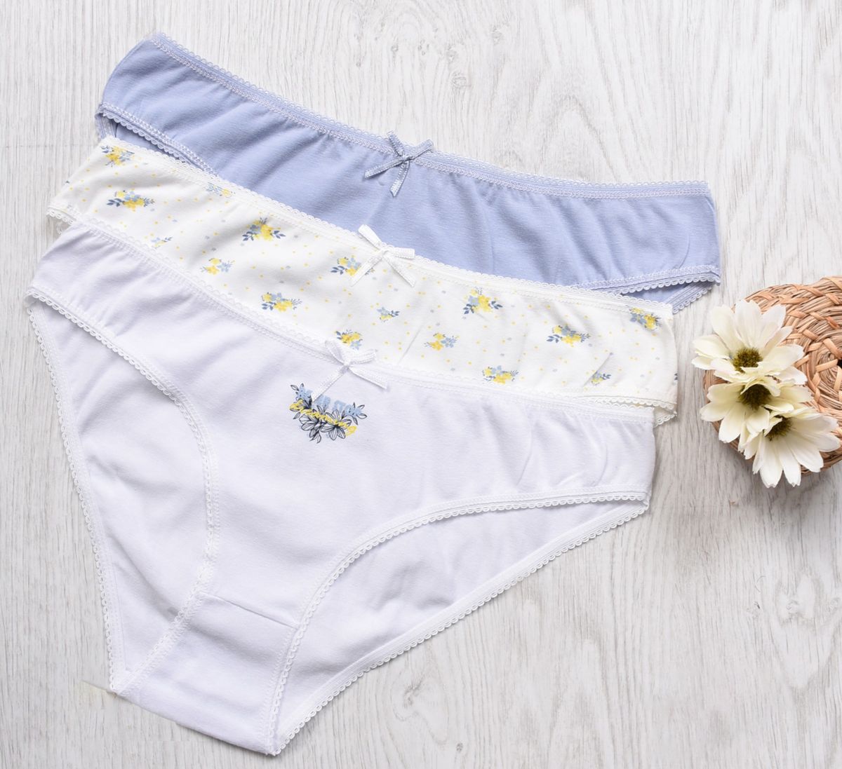 Three pairs of cotton underwear in white, pale blue, and a small floral print, laid out on a light wooden surface