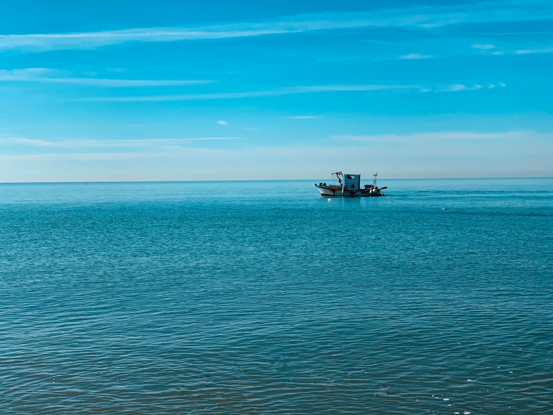A lone fishing boat sails on the calm Mediterranean Sea under a clear blue sky in Fregenae, Italy.