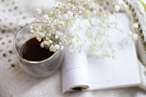 White Flowers Over a Cup of Drink and Open Book
