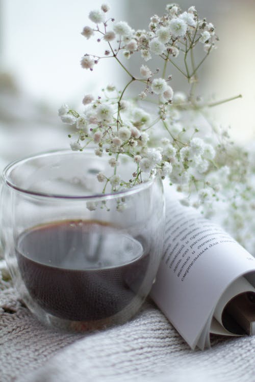 Tea in a Glass Cup and Rolled Book Pages Near a White Flower