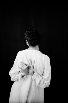 A mysterious woman standing in a studio gesturing with her hands, captured in a black and white photograph.