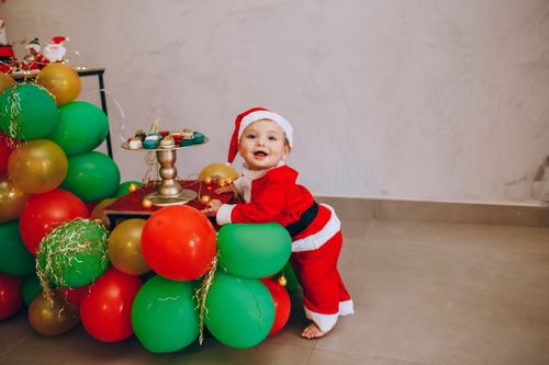 Free Cute baby dressed as Santa surrounded by colorful balloons, perfect for holiday celebrations. Stock Photo