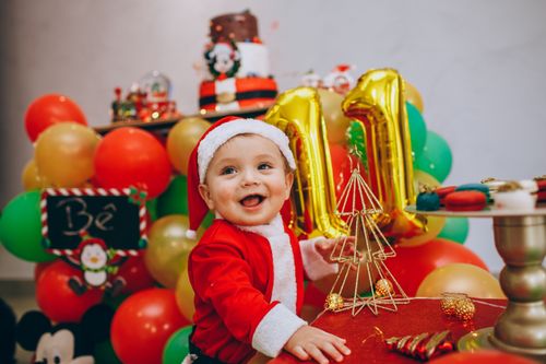 Free Adorable baby wearing Santa costume enjoying a colorful festive setting with balloons and Christmas decorations. Stock Photo
