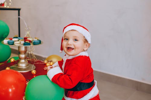 A Toddler in Santa Costume Playing with a Green Balloon