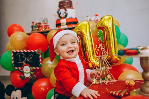 A Cute Toddler in Santa Costume Playing with a Christmas Ornament