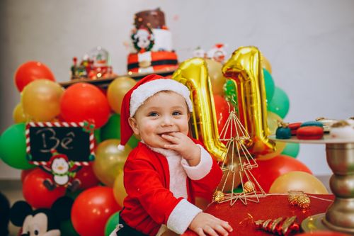 Free Cute baby in Santa outfit surrounded by colorful balloons at a festive party. Stock Photo