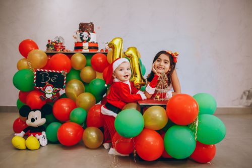 Free A joyful indoor birthday celebration featuring children in Santa outfits surrounded by festive balloons and decorations. Stock Photo