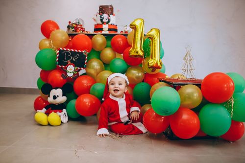 Free A joyful baby dressed as Santa amidst colorful Christmas balloons and decorations. Stock Photo