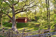 在阳光明媚的夏日景色中，坐落着一座田园诗般的瑞典红房子，四周绿树成荫，围着木栅栏