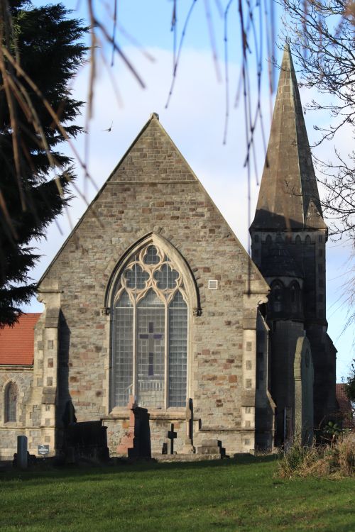Free A stunning medieval church with Gothic architecture, featuring a tall spire and stained glass window, surrounded by greenery. Stock Photo
