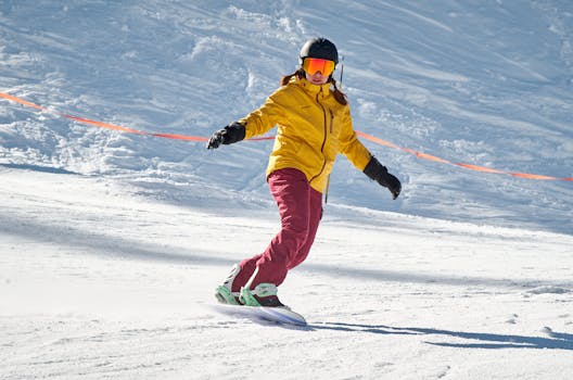 A snowboarder in a yellow jacket and red pants rides down a snowy slope on a sunny winter day.