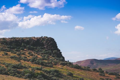 Free Beautiful countryside with a rocky cliff under a vibrant blue sky and scattered clouds. Stock Photo