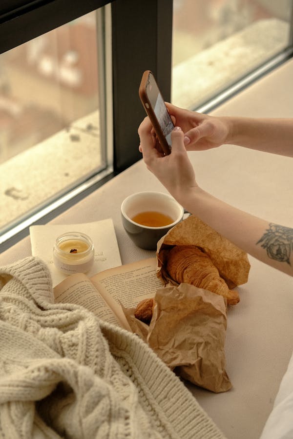Unrecognizable Hands Checking Messages on Mobile Phone at Window Sill at Home