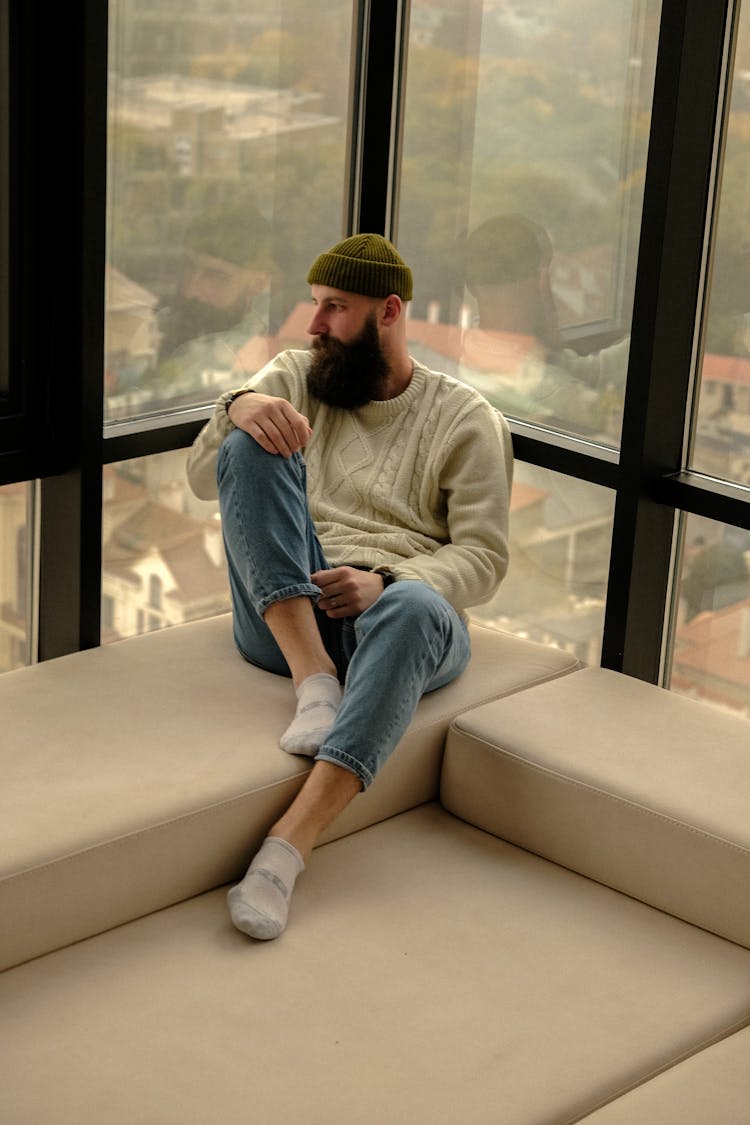 Man In Hat With Black Beard Sitting Comfortably By Window In Corner Of Office Building