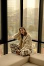 Woman Wearing Big Cardigan and Checkered Pants Sitting Crossed Legged by Office Window