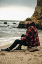 Bearded Man in Knitted Hat Sitting on Sandy Beach and Looking at Sea