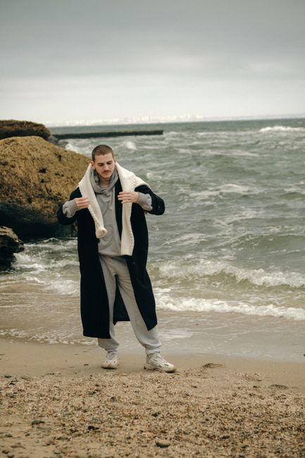 Portrait of a young man in a long coat by the seashore on a cloudy day.