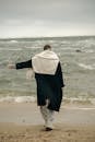 Unrecognizable Man Wearing Black Coat Standing on Beach with Stretched Arm to Side