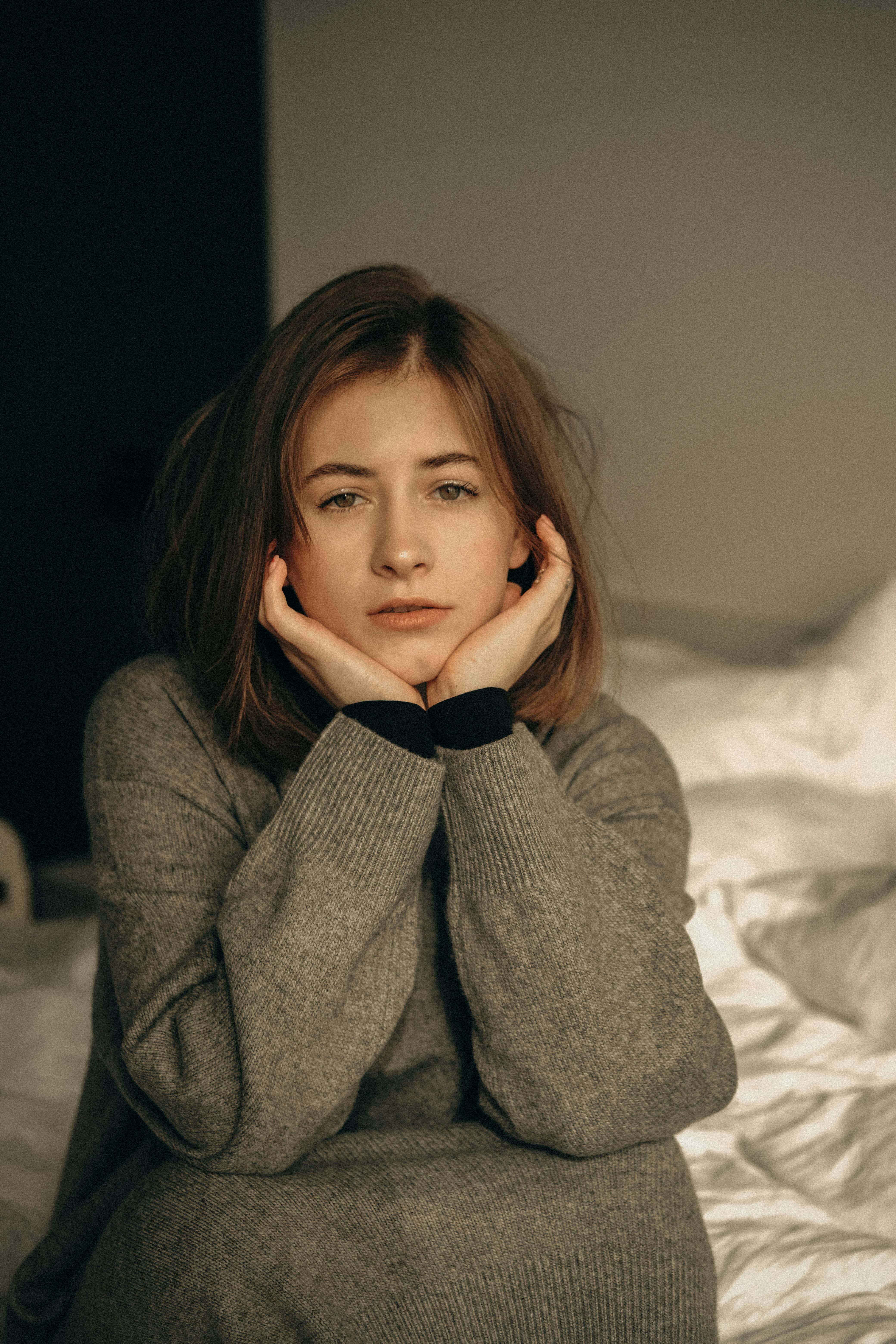 young woman looking tired sitting on bed with head resting on hands