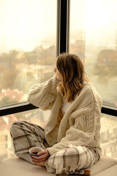 Cross Legged Sitting Woman Holding Cup of Tea Looking Through Window