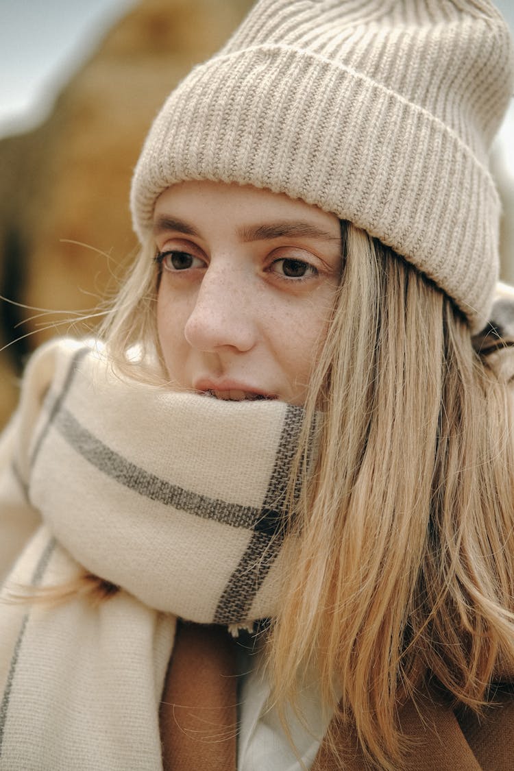 Young Blond Woman In Beige Knitted Hat And Warm Shawl Wrapped Around Her Mouth