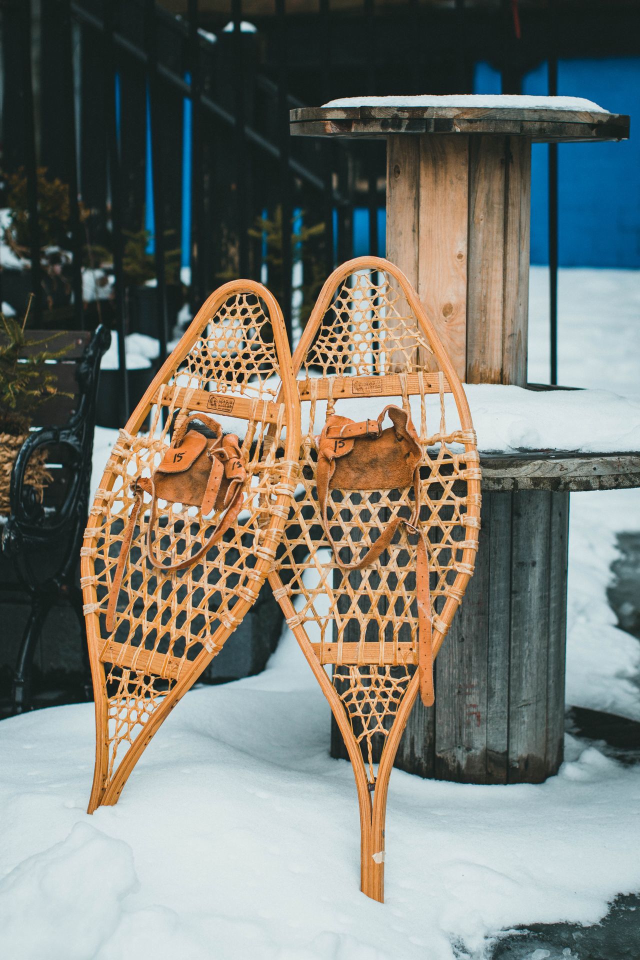 Vintage wooden snowshoes with leather bindings leaning against a wooden post in deep snow.