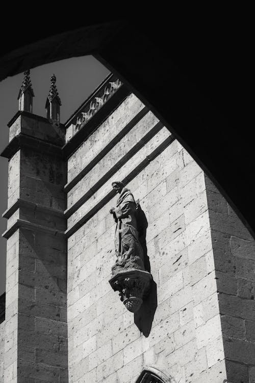 Grayscale Photo of Man Statue on Exterior Concrete Wall of a Building
