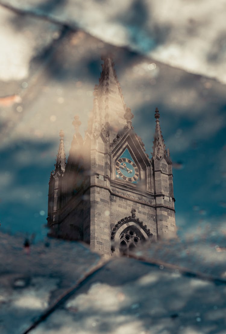 A Reflection Of A Gray Concrete Cathedral Tower With Clock On Water