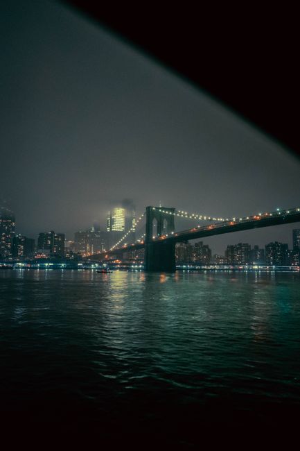 Stunning nighttime view of Brooklyn Bridge illuminated over New York City's skyline reflecting on the water.