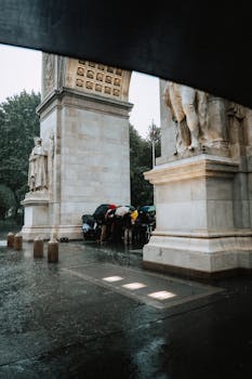 Tourists with umbrellas gather under Washington Square Arch during a rainy day in New York City.