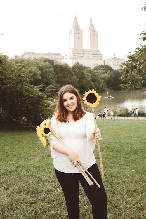 Free A Woman in White Top Holding Sunflowers Stock Photo