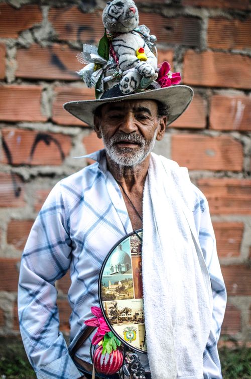 Free A senior man with a unique toy-decorated hat stands against a rustic brick wall. Stock Photo