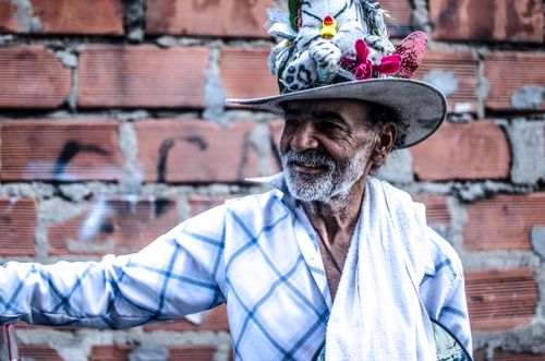 Free Charming senior man with unique hat smiling joyfully in front of a brick wall. Stock Photo
