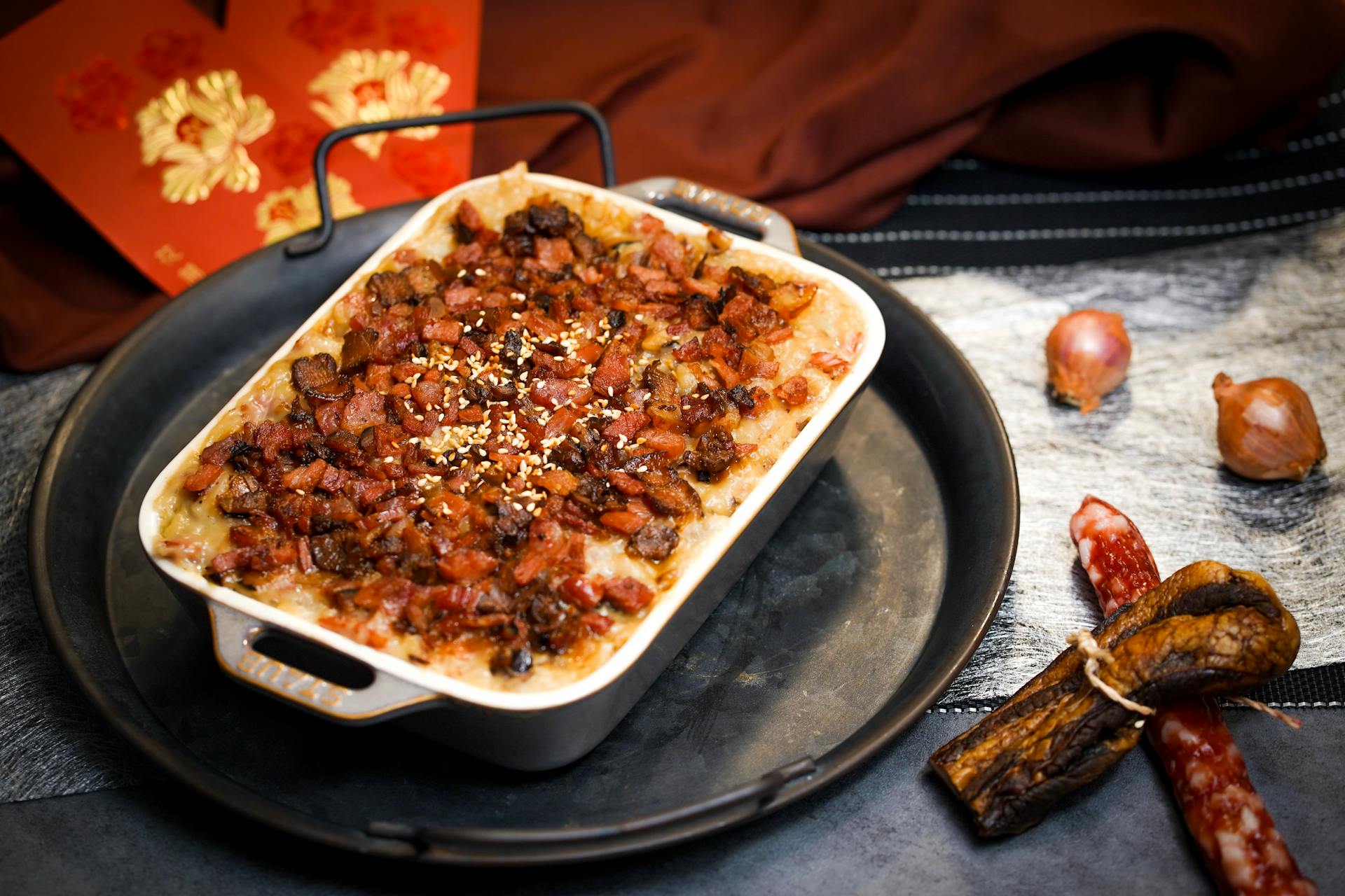 Close-up of a savory Asian baked dish topped with Chinese sausage, garnished with sesame seeds, showcasing ingredients.