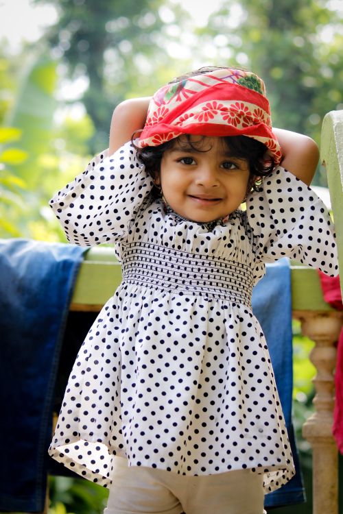 Free Charming portrait of a smiling girl in a polka dot dress and floral hat enjoying the outdoors. Stock Photo