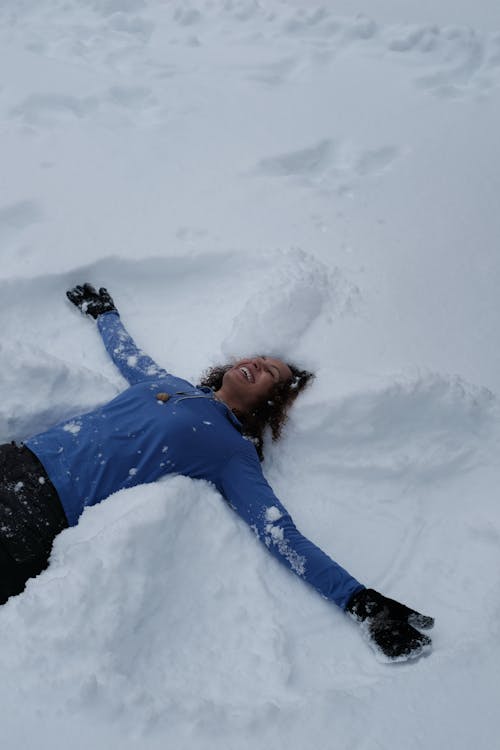 A Woman in Blue Long Sleeves Lying on a Snow Covered Ground