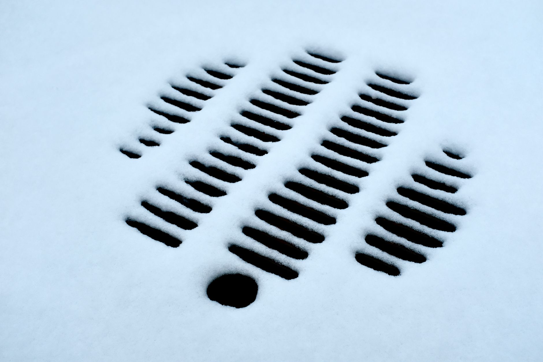 Close-up of a snow-covered drain grate highlighting winter's cold and abstract patterns.